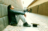 person sitting against wall with hat on ground to catch change