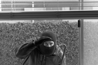 person in balaclava with crowbar looking through window