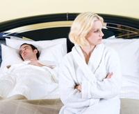 two people in bed, one wears robe and looks unimpressed