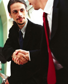 two people wear suits and shake hands