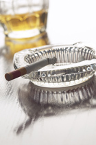 a crooked cigarette in an ashtray, glass of alcohol behind